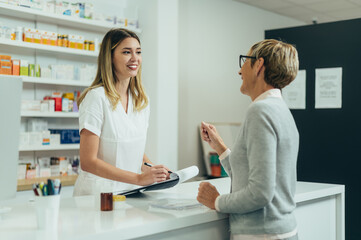 Obraz premium Happy senior woman customer buying medications at drugstore while talking with a female pharmacist