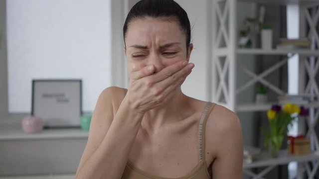 Young slim vegetarian woman with nausea looking at raw meat indoors. Portrait of fit beautiful Caucasian lady vomiting holding uncooked beef steak. Vegetarianism concept