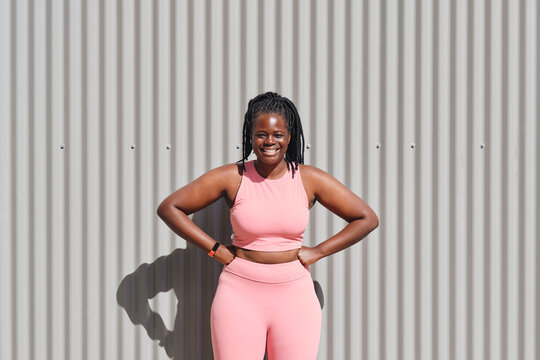 Happy curvy young woman with hands on hips in front of corrugated wall