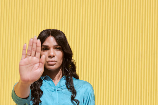 Non-binary woman showing stop gesture in front of yellow wall