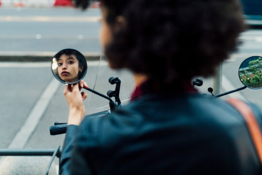 Woman looking at side-view mirror of motor scooter