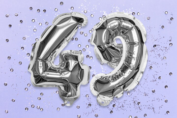 Silver foil balloon number, digit forty nine on a lilac background with sequins. Birthday greeting card with inscription 49. Top view. Numerical digit. Celebration event, template.