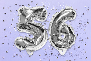 Silver foil balloon number, digit fifty six on a lilac background with sequins. Birthday greeting card with inscription 56. Top view. Numerical digit. Celebration event, template.