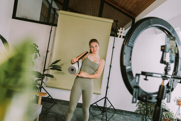 Female fitness trainer showing exercise mat while vlogging at home