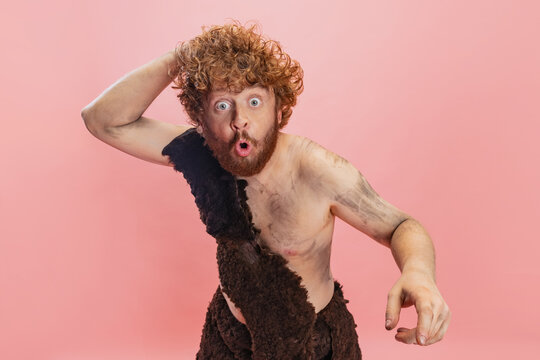 Cropped portrait of man in character of neandertal scratching back of his head isolated over pink background