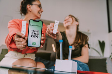 Female friends showing testing kit and smart phone with COVID-19 tracking app at home