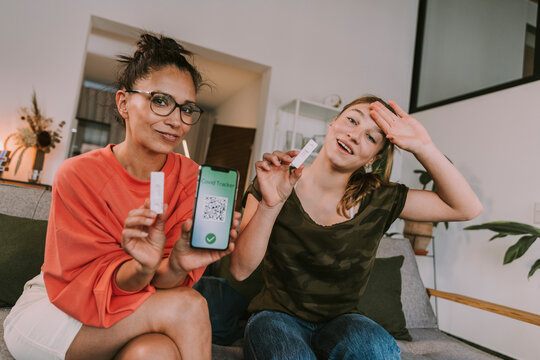 Woman showing COVID-19 tracker on smart phone near girl holding test kit at home