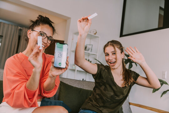 Happy female friends showing negative COVID-19 result on smart phone at home