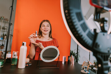 Smiling female influencer presenting lipstick during make-up tutorial filming at home