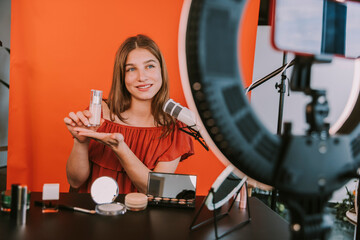 Smiling female influencer presenting foundation while filming make-up tutorial at home workshop