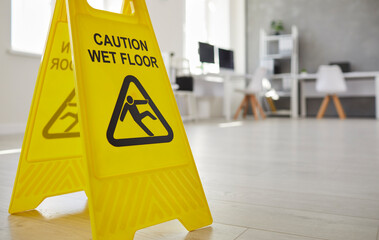 Cleaning. Close up of yellow plastic standing safety sign warning us about wet slippery office...