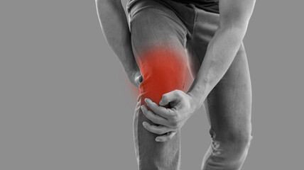 Man who hurt his knee is touching red inflamed area. Gray banner background with cropped black and white shot of young guy feeling acute pain in knee cap. Arthritis, osteoarthritis, rheumatism concept