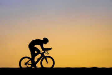 Male triathlete riding bicycle during sunset