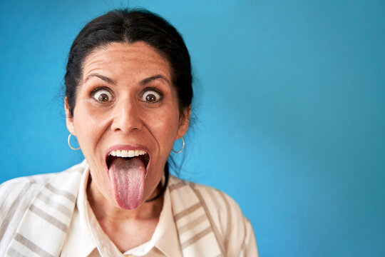 Mature woman sticking out tongue in front of blue wall
