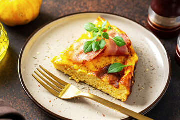 A piece of frittata with pumpkin, bacon and ricotta in a ceramic plate on a dark culinary background. Traditional Italian delicious homemade egg dish on the kitchen table