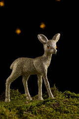 Close-up of Christmas deer on green moss and black background with lights, vertical