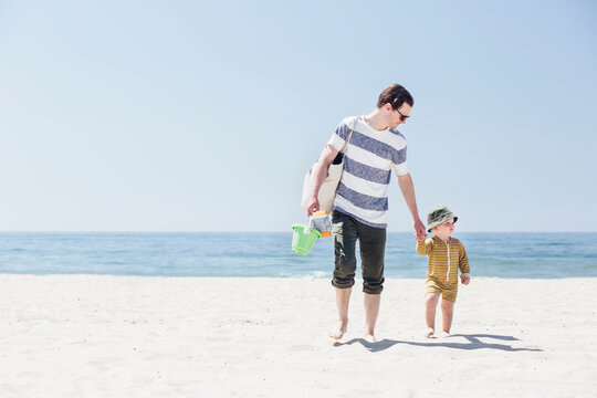 Father and son holding hands while walking at beach