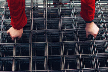 Closeup hands of a worker holding stainless steel mesh, rebar or building grid at factory, plant or...