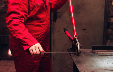 Worker wearing red overalls using pincers or plier wrenches to cut a steel wire or bar in workshop...