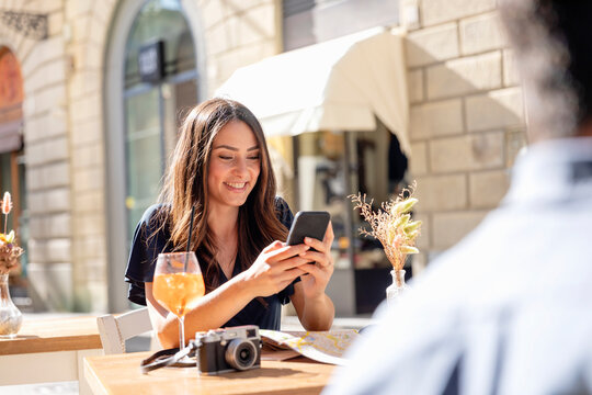 Smiling woman using mobile phone while sitting at sidewalk cafe