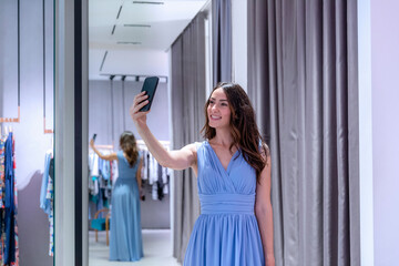 Woman taking selfie while wearing blue dress near changing room in boutique