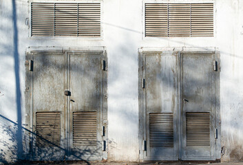 2 old rusted metal doors in the white concrete wall of electric transformer building