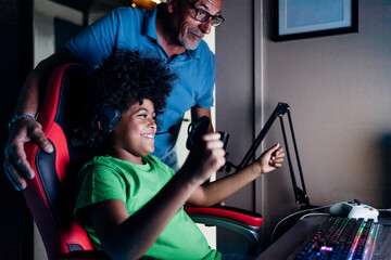 Cheerful boy celebrating victory with grandfather while playing video game at home