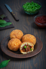 Homemade Arancini italian rice balls, coated with bread crumbs, deep fried and stuffed with minced meat and green peas served on plate with tomato sauce and knife on dark brown wooden background