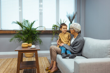 In cozy embraces of grandma. Adorable boy grandchild relax on couch in loving granny arms listen to stories wise advices. Smiling preteen boy feel emotional bonding with caring aged female custodian
