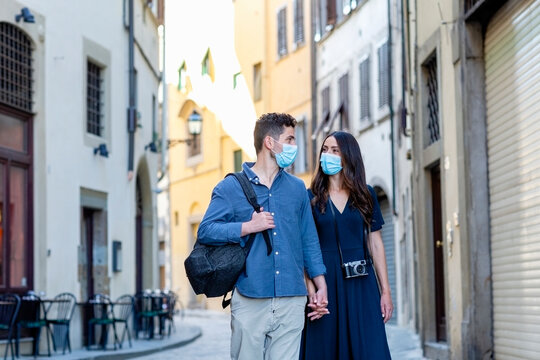 Tourist couple with protective face mask holding hands while walking on city street