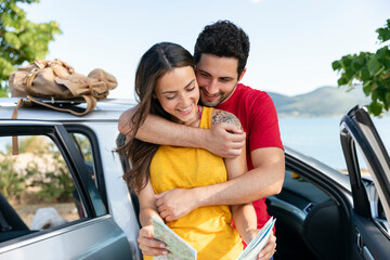 Boyfriend embracing girlfriend holding map by car