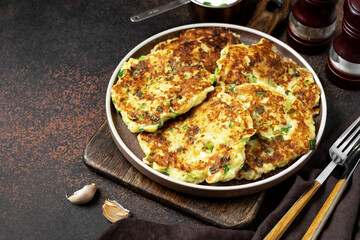 Homemade potato pancakes with cottage cheese and green onions in a ceramic plate on a dark background. A traditional dish of European cuisine from vegetables in close-up	