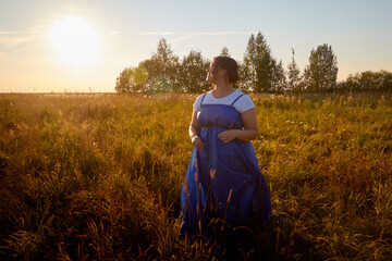 Peasant plump chubby pleasant woman in green grass field. Girl in blue old russian dress posing outdoors in nature in a day or a evening