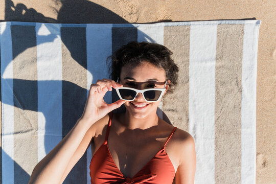Smiling young woman wearing sunglasses while lying on towel at beach