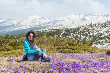 Beautiful Woman Sitting in a High Snowy Mountain with Blooming Purple Crocuses .Winter Vacation in Bulgaria ,Seven Rila Lakes 