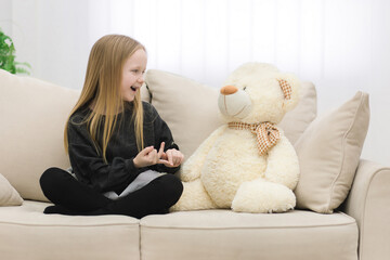 Photo of little girl playing with white teddy bear.