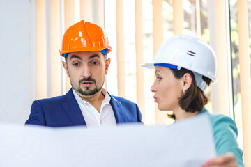 Photo of two engineers wearing helmets and holding paper with plan.