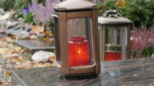 Red memorial candle burning with fire on rainy day on tombstone in cemetery autumn, rainy day. Grave with tombstone on which raindrops falling, against abackground of yellow foliage. Day of all dead