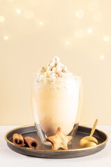 Christmas eggnog with foam of whipped cream with cinnamon in glass on metallic plate on beige.