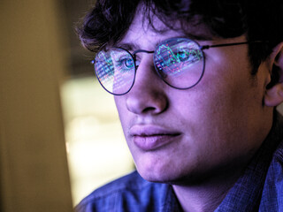 Male teenager with stock market data reflection on eyeglasses