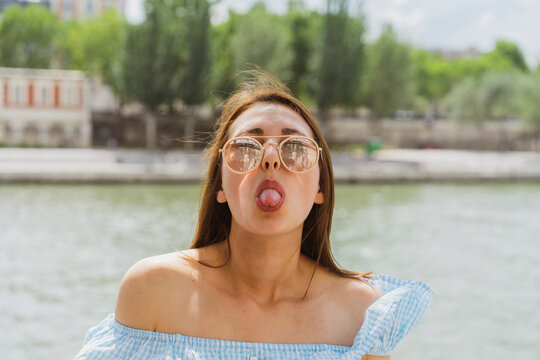 Woman wearing sunglasses sticking out tongue in front of river