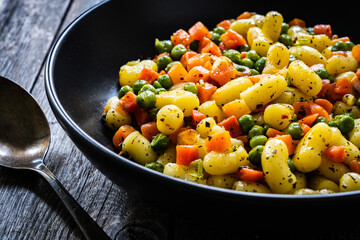 Gnocchi with green peas and carrots on wooden table
