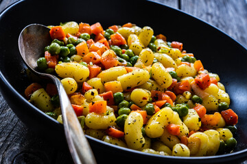 Gnocchi with green peas and carrots on wooden table
