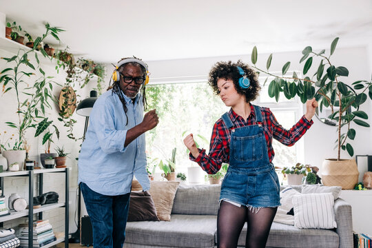 Young woman listening music through headphones while dancing with father at home