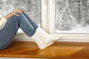 Woman legs with warm socks and winter window background 