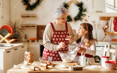 Cute little girl helping senior grandmother to make dough for traditional Christmas cookies