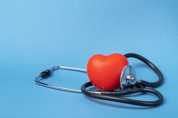 Stethoscope and rubber red heart on a blue background with space for text. Heart health, healthcare concept.