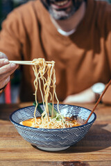 Handsome mature man eating ramen with chopsticks in an asian restaurant