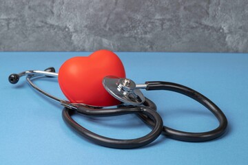 A stethoscope and a rubber red heart on a blue table against a gray marble wall. Heart health, healthcare concept. Heart health, healthcare concept.