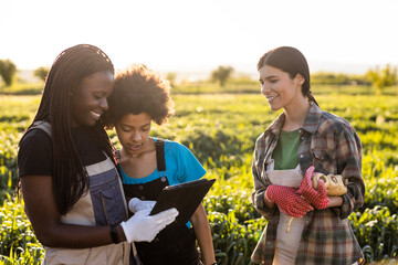 Mother and daughter discussing over digital tablet while standing by female colleague at farm